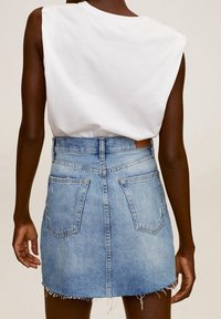 Persona que lleva una blusa blanca sin mangas metida en una falda corta de mezclilla blanca de tiro alto con el dobladillo deshilachado y bolsillos traseros.