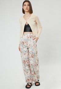 Light beige cardigan with a single button, paired with white floral-patterned wide-leg trousers featuring pink and blue flowers. Black sandals.