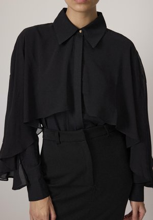 Black blouse with a high collar, structured bodice, and layered sheer sleeves. Features a single gold button at the neck.