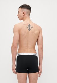 Black boxer shorts with white "SELECTED" logo waistband, smooth fabric, fitted design, and a visible tattoo on the upper back.