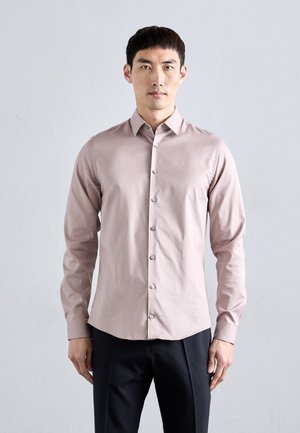 Chemise à manches longues rose clair avec un devant à boutons et une coupe ajustée. Tissu lisse, col pointu et boutons argentés. Associée à un pantalon foncé.