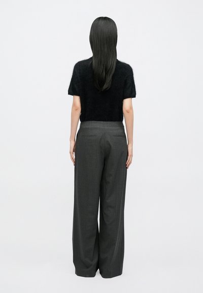 Μαύρο χνουδωτό πουλόβερ με κοντά μανίκια συνδυασμένο με γκρι παντελόνι φαρδιάς γραμμής με λεπτές ρίγες. Έντονες κάθετες γραμμές στο ύφασμα, χαλαρή σιλουέτα.