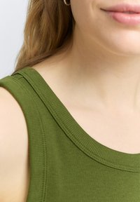Olivgrön ribbad tanktop med bred ringning och subtila sömdetaljer, visad mot en neutral bakgrund. Mjuk textur är synlig.