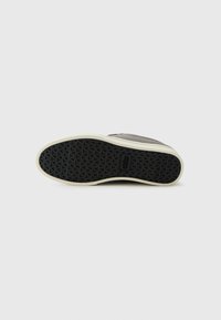 Sneaker with a dark gray upper made of fabric, a textured black rubber sole, and a white midsole, featuring a patterned grip design.