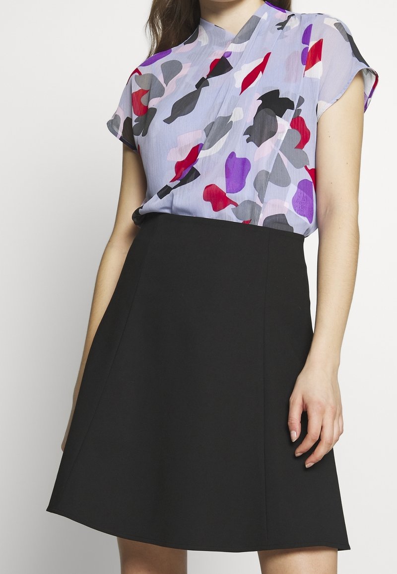 Top holgado de manga corta con un fondo de color púrpura claro, que presenta formas abstractas en rojo, gris y negro. Combinado con una falda negra tipo A.