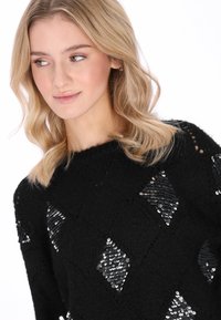 Fekete kötött pulóver, elöl rombusz alakú flitteres díszítéssel, texturált felülettel és kerek nyakkivágással.
