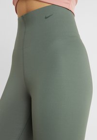 Legginsy z wysokim stanem w kolorze mchu, wykonane z gładkiego materiału. Posiadają subtelną logo Nike w górnym lewym rogu.