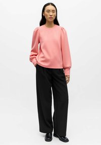 Roze sweatshirt met pofmouwen, ronde hals, gecombineerd met zwarte wijde broek en zwarte schoenen. Soepele textuur, casual pasvorm.