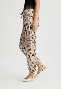 Lett, mønstrede joggingbukser i beige med brune leopardpletter; elastisk talje med snor; sidelommer; afsluttede ankler.