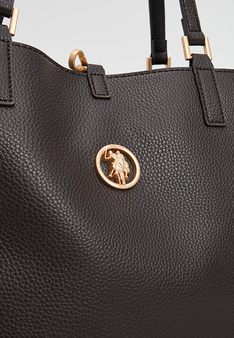Braune, strukturierte Lederhandtasche mit goldfarbenen Beschlägen und einem kreisförmigen Emblem mit detailliertem Design. Zwei Griffe zum Tragen.