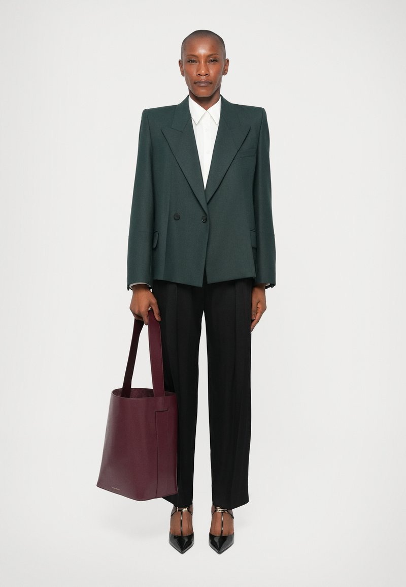 Blazer vert à double boutonnage, chemise blanche, pantalons plissés noirs et sac fourre-tout bordeaux. Escarpins noirs brillants à bouts pointus.