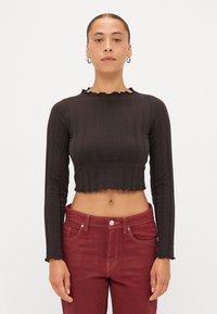 Sort ribbet crop top med lange ærmer, der har en blødt bølget halsudskæring og kant. Sammen med burgunder højttaljede jeans.