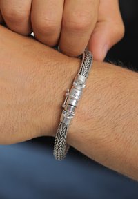 Silver braided bracelet with a cylindrical clasp, featuring engraved detailing, worn on a wrist with light hair.