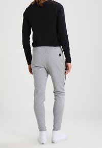 Graue Baumwoll-Sweathosen mit schmalem Schnitt, seitlichen Taschen und schwarzen Akzenten. Kombiniert mit einem schwarzen Langarmoberteil und weißen Turnschuhen.