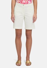 Białe szorty do kolan z podwiniętymi mankietami i kieszeniami z przodu. Wykonane z gładkiego, lekkiego materiału. Na dole widoczne złote sandały.