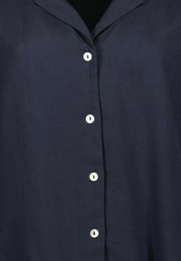 Camicia blu navy con una trama liscia, dotata di un colletto a margine e sei bottoni bianchi lungo la patta anteriore.