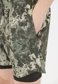 Groene en beige gestreepte sportshorts met een elastische tailleband en zijzakken, gelaagd over een zwarte strakke onderkleding, met een gestructureerde stof.