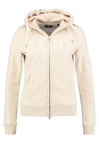 Felpa beige con zip e cappuccio regolabile, tasche frontali, polsini a coste e il testo "GANT" sul petto.