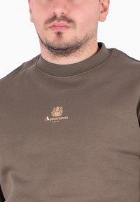 Ciemnobrązowa bluza z okrągłym dekoltem wykonana z bawełny o gładkiej teksturze. Posiada złote logo z napisem "Aquascutum ACTIVE" na klatce piersiowej.