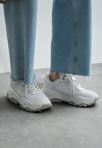 Hvite sportssko med teksturerte strikkede overflater og polstrede såler. Kombinert med lyseblå jeans med frynsete kanter.