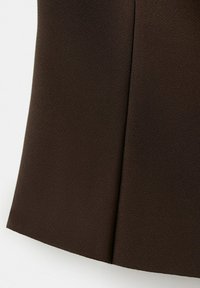 Tissu texturé marron foncé avec une couture centrale, tombant en douceur sur un fond clair.