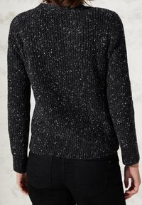Czarny prążkowany sweter z białymi drobnymi plamkami, o dopasowanym kroju, długich rękawach i teksturowanej powierzchni. Widok od tyłu podkreśla jego design i kształt.