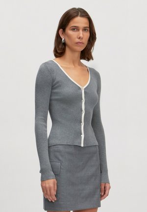 Grijze geribbelde cardigan met V-hals, witte knopen sluiting en lange mouwen, gecombineerd met een bijpassende grijze rok met zijzakken.