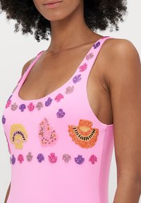 Fato de banho rosa com detalhes decorativos em pérolas e lantejoulas em várias cores e formas, incluindo flores e leques, na parte da frente.