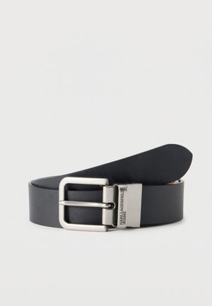 Fekete bőr öv ezüst téglalap alakú csattal, melyen a "Karl Lagerfeld Jeans" logó gravírozva van, egy világos háttér előtt feltekerve.
