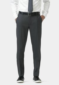 Pantalon gris en tissu texturé, présentant une coupe ajustée et un pli avant. Associé à des baskets noires et une chemise blanche.