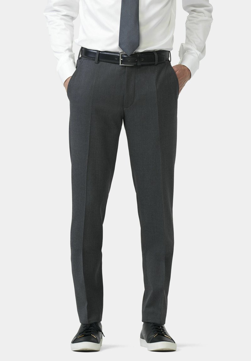 Pantalon gris en tissu texturé, présentant une coupe ajustée et un pli avant. Associé à des baskets noires et une chemise blanche.