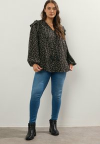 Blusa nera a fiori con maniche a frufru, scollatura a V, dettagli con frange; abbinata a jeans skinny blu chiaro e stivaletti neri.