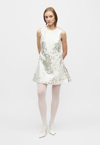 Rochie fără mâneci de culoare argintie deschisă, cu un model floral texturat, croială evazată, lungime până la genunchi, purtată cu colanți albi și pantofi cu vârf ascuțit.