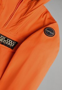 Manche de veste orange vif avec des écussons de la marque Napapijri noirs et beiges sur le haut du bras et la poitrine.