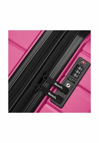 Valigia rigida rosa con cerniere nere e doppi cursori etichettati "Bench", caratterizzata da una combinazione di serratura nera e superficie testurizzata.