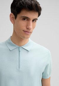 Jasnoniebieska krótko rękawowa koszulka polo z zamkiem błyskawicznym przy szyi. Wykonana z miękkiego materiału o gładkiej teksturze. Posiada klasyczny kołnierzyk i dopasowany krój.