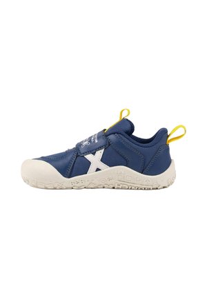 Zapatilla infantil azul marino con suela blanca texturizada, "X" blanco en el lateral, tiradores amarillos y cierre de velcro sobre fondo blanco liso.