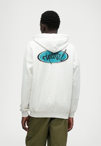 Hall kehaga kapuutsiga hall särk, mille tagaküljel on sinine ovaalne logo musta kirjatüübiga. Ribiga alläär ja varrukad, pehme tekstiilimaterjal.