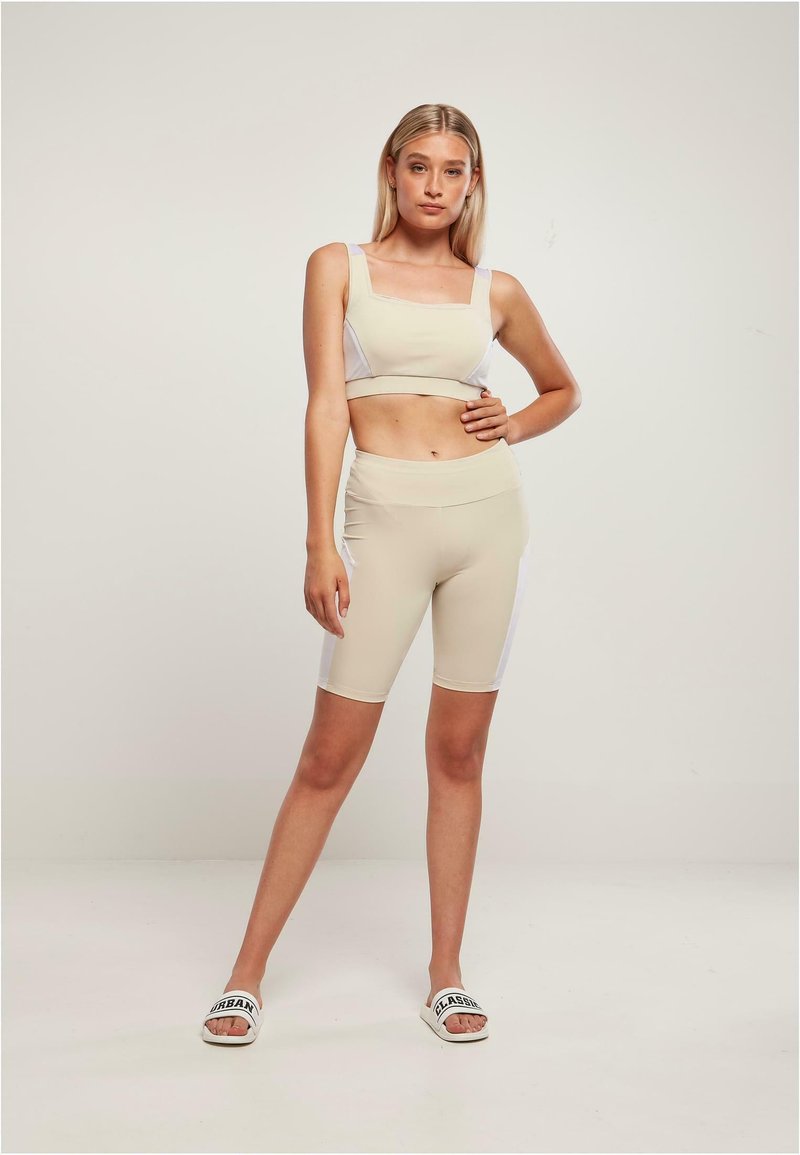 Bajer sportski crop top bez rukava s kvadratnim izrezom u kombinaciji s odgovarajućim bež biciklističkim šortsevima visokog struka. Bijeli bočni naglasci.