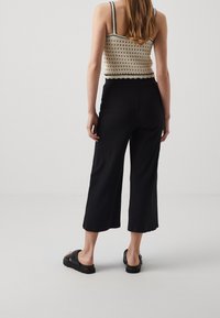 Pantalon culotte noir à côtes avec une coupe large, associé à un top court en tricot beige avec un ourlet festonné et des bretelles fines.