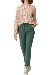 Blusa floral de manga larga con escote en forma de llave, combinada con pantalones tipo cargo verdes que cuentan con bolsillos laterales y un ajuste relajado.