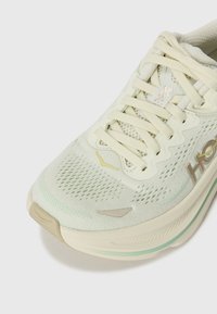 Sapatilha de corrida verde claro com parte superior em malha, atacadores planos e sola acolchoada. Apresenta pormenores subtis em dourado e biqueira texturizada.