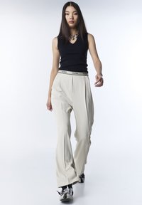 Top negro sin mangas con escote en V, combinado con pantalones de pierna ancha color crema con una cinturilla negra de marca y zapatillas con detalles plateados.