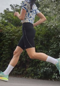 Black cycling shorts with a high waistband, paired with a blue and white patterned athletic top. The individual is wearing mint-colored running shoes.