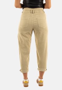 Beige ribfluweel broek met een hoge taille, ceintuurlussen en opgerolde boorden. Heeft twee achterzakken en een gestructureerde ribbelstof.