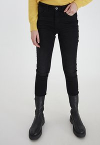 Fekete, slim fit szabású farmernadrág, magas derékkal, öt zsebes dizájnnal és gombos záródással, fekete bokacsizmával párosítva.