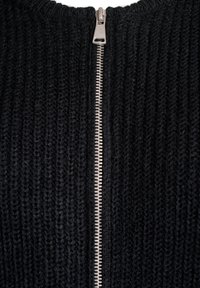 Black knitted sweater featuring a central metal zipper, ribbed texture, and rounded neckline. The zipper extends from the neck to the hem.