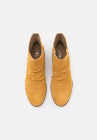 Botines amarillos perforados con un diseño arrugado. Presentan un material suave y una suela plana. Cremalleras laterales para facilitar su uso. Talla 38.