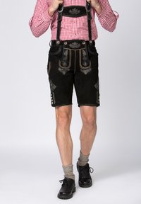 Musta nahkainen lederhosen, jossa on kirjailtu koristelu, säädettävät olkaimet, etutaskut ja koristeelliset napit. Yhdistetty harmaisiin polvisukkiin ja mustiin kenkiin.