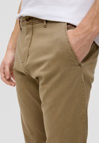 Khakihosen mit glatter Textur, geradem Bein und Seitentaschen. Mit einem Knopfverschluss am Taillenbund.